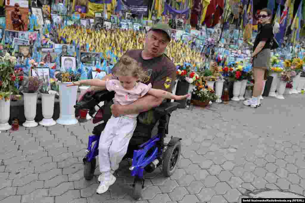 Ветеран на візку із дівчинкою на руках поруч із народним меморіалом Майдані Незалежності в Києві. Липень 2025 року