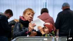 O alegătoare se pregătește să arunce buletinele în urna de vot în cadrul alegerilor prezidențiale și referendumului din 20 octombrie.