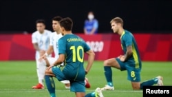 Az argentin és az ausztrál válogatott tagjai fél térdre ereszkednek a 2021-es tokiói olimpia egyik első labdarúgó-mérkőzésén