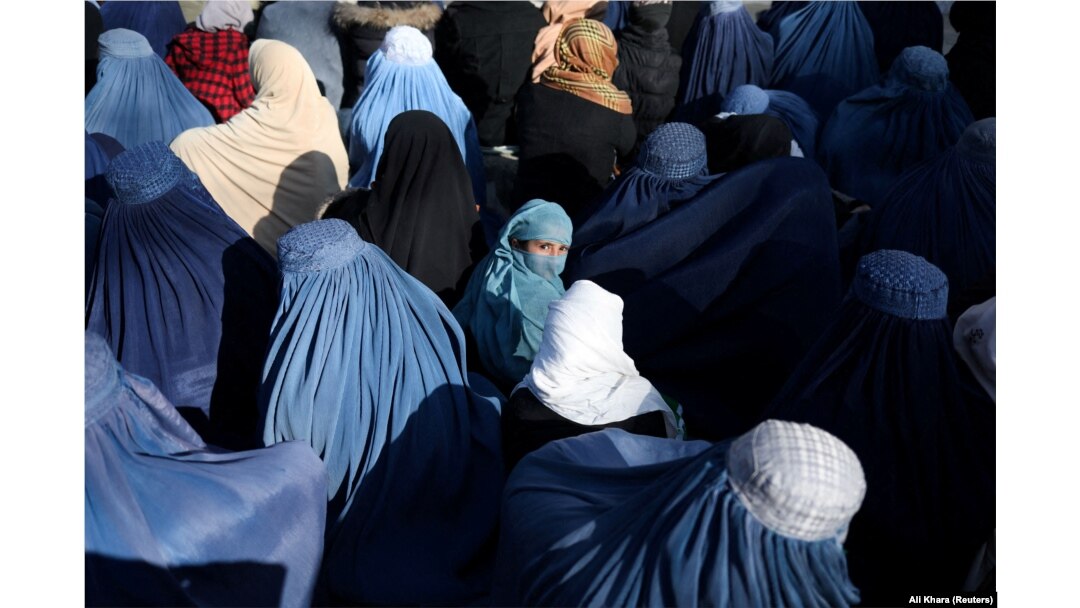 A girl sits in front of a bakery in a crowd of Afghan women waiting to receive bread in Kabul.