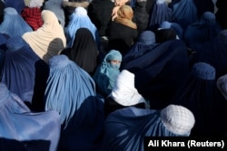 A girl sits in front of a bakery in a crowd of Afghan women waiting to receive bread in Kabul.