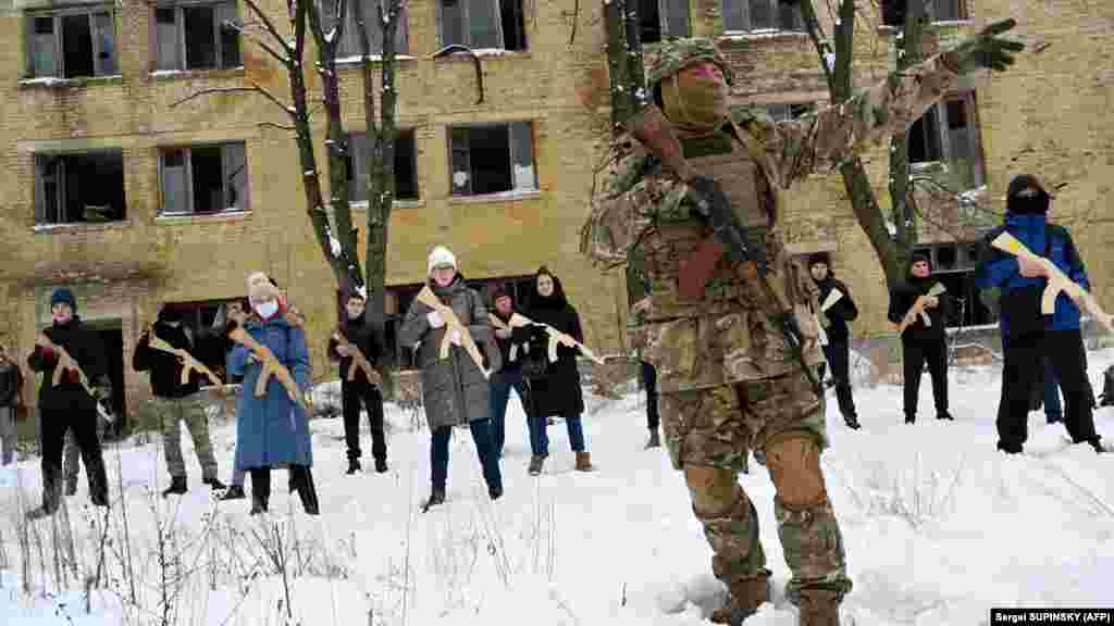 Un instructor militar îi învață pe civili cum să folosească puști de asalt Kalașnikov, la o sesiune de antrenament desfășurată la o fabrică abandonată din capitala Ucrainei, Kiev. Civilii exersează cu puști din lemn. 30 ianuarie, 2022 &nbsp;