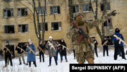Civili ucrainieni antrenându-se cu puști Kalașnilov de lemn în spațiul unei fabrici abandonate de la Kiev. 30 ianuarie 2022. Instrucția presupune și tehnici de prim-ajutor, curse cu obstacole și tactică militară.