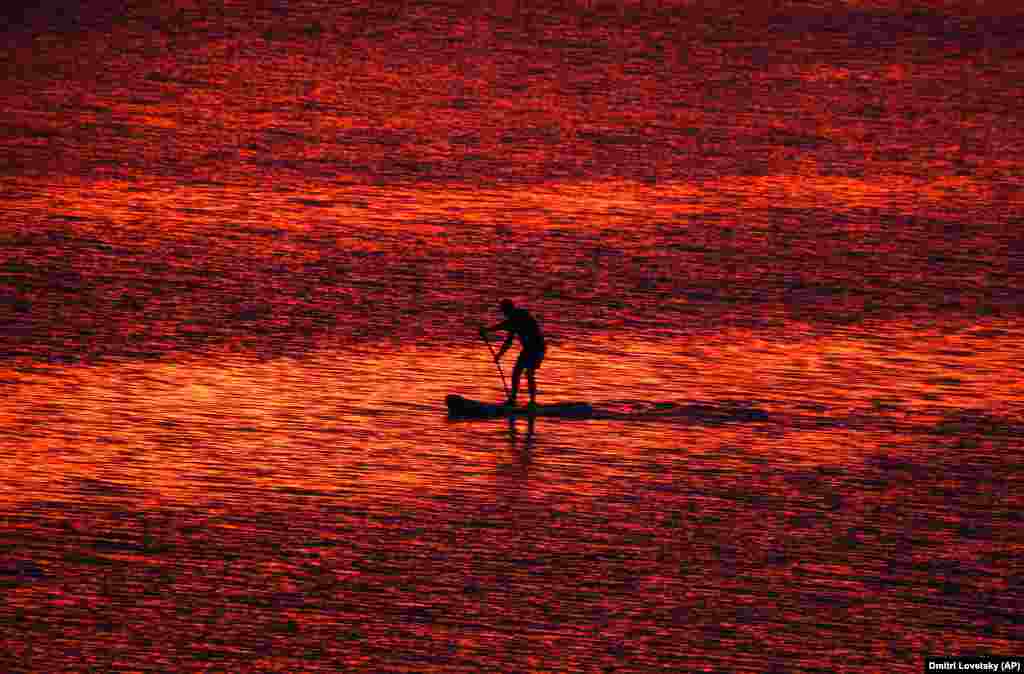 A man steers his stand-up paddleboard at sunset on the Velikaya River in Pskov, southwest of St. Petersburg. (AP/Dmitry Lovetsky)