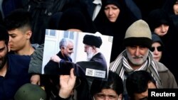 A man holding a picture of Qassem Soleimani and Supreme Leader Ali Khamenei during the march against the Qods Force commander's killing. 