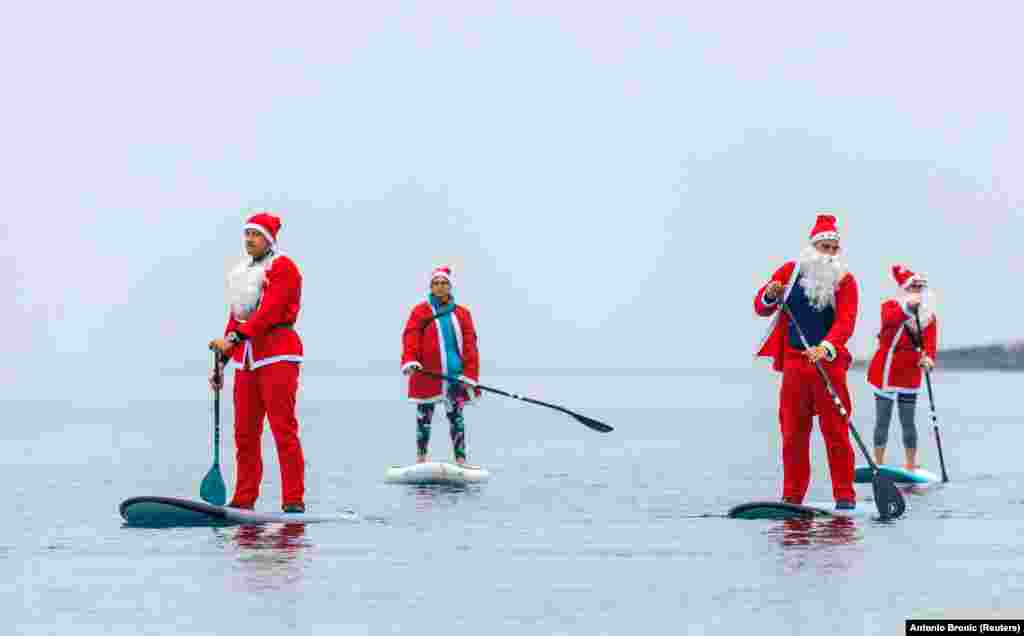 Mikulásruhába öltözve paddleboardoznak, vagyis egy eveződeszkán szörföznek ezek az emberek Horvátországban december 23-án.