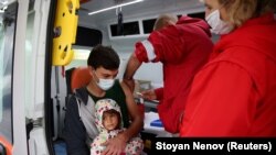 Човек ја држи својата ќерка, додека ја прима втората доза вакцина против коронавирус што ја дава медицински персонал од мобилната единица во селото Крушовица, Бугарија, 10 октомври 2021 година.