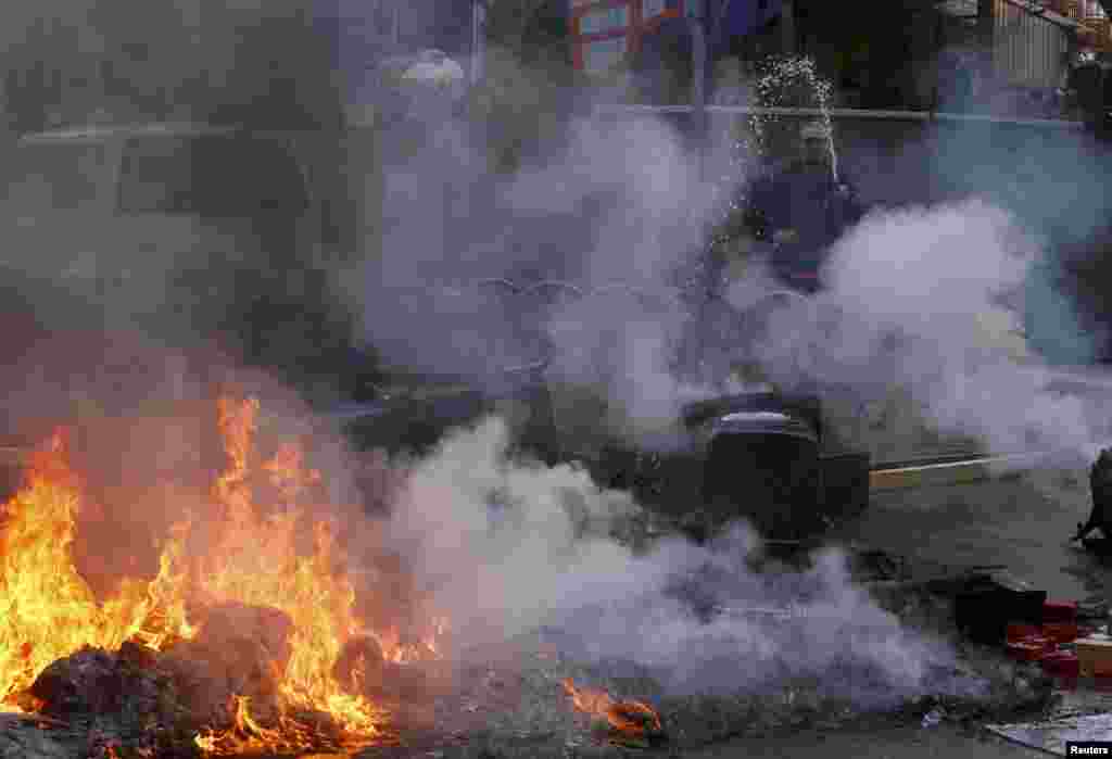 Местный житель тушит горящую баррикаду, устроенную митингующими