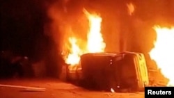 Преобърната кола гори пред полицейски участък в Азна. Снимката е от видеоклип, публикуван в социалните мрежи на 1 януари 2026 г.