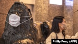 Maszkos nő az ugyancsak maszkos oroszlánszobor előtt Tokió bevásárlónegyedében, Ginzában az omikron első megjelenése után Japánban, 2022. január 18-án