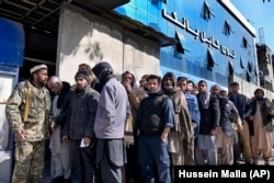 A Taliban fighter stands guard in front of people waiting to enter a bank in Kabul.