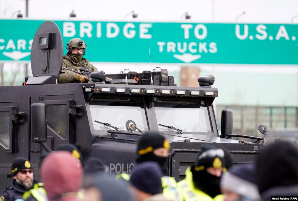 Policia kanadeze në përpjekje për të shpërndarë protestuesit, që bllokuan hyrjen në një urë në Ontario të Kanadasë. Protestat në këtë vend kanë hyrë në javën e tretë dhe kanë frymëzuar veprime të ngjashme në disa vende të botës. (AFP)