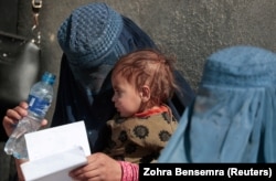 A displaced woman holds her child as she waits with other women to receive aid outside a UN distribution center on the outskirts of Kabul in October.