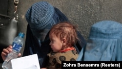 A displaced Afghan woman holds her child as she waits to receive aid supplies outside a UNCHR distribution center on the outskirts of Kabul. 