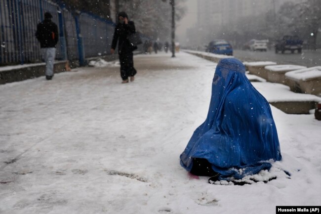 Një grua afgane me burka, e ulur në borë, duke kërkuar lëmoshë. Kabul 2022.