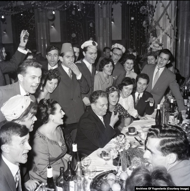 Иосип Броз Тито курит трубку в окружении гостей на вечеринке в Белграде в 1960 году. Гости поют.