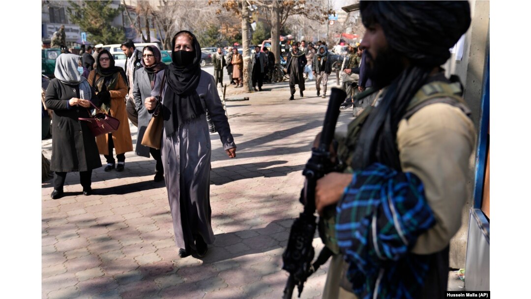 Afghan women pass by a Taliban fighter on a street in Kabul.
