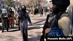 Afghan women pass by a Taliban fighter on a street in Kabul.