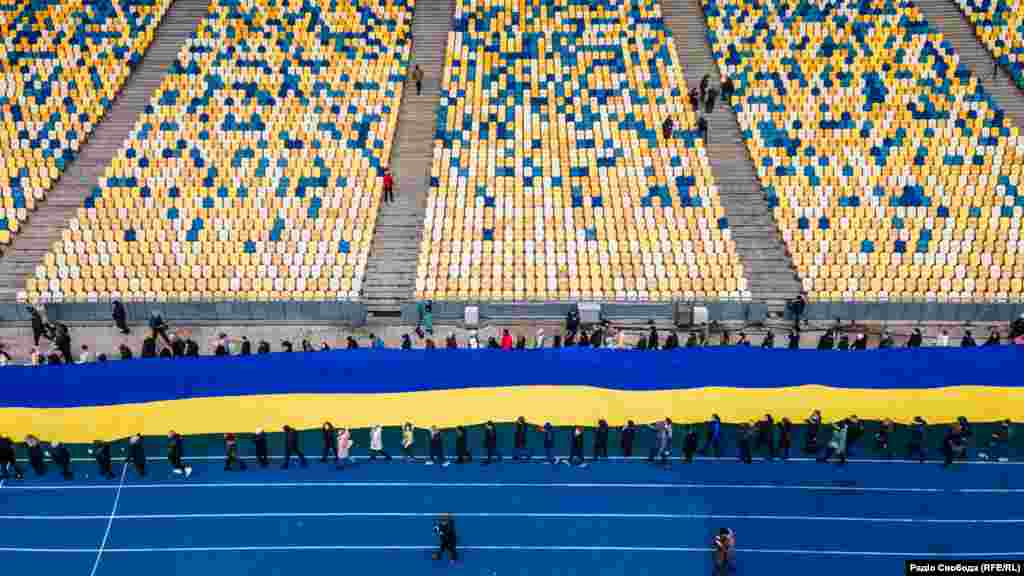 У Києві на НСК &laquo;Олімпійський&raquo; до Дня єднання відбулася акція, на якій активісти розгорнули найбільший державний прапор у столиці&nbsp;&ndash; 200 метрів завдовжки. Участь у акції взяли декілька сотень людей. Учасники акції пройшли із прапором декілька кругів навколо поля стадіону. Хода супроводжувалася піснею Тараса Петриненка &laquo;Україна&raquo;. Київ, 16 лютого 2022 року