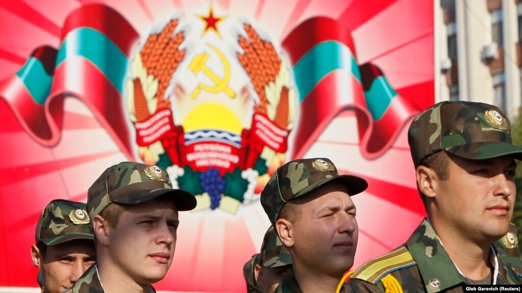 Войници от самообявилата се Приднестровска молдовска република (ПМР) по време военен парад в Тираспол през 2012 г. Зад тях е гербът на ПМР.