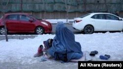 An Afghan woman holding her child begs on a snow-covered sidewalk in Kabul.