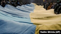 Oameni purtând un steag ucrainean de mari dimensiuni pentru a marca „ziua unității” decretată de președintele Ucrainei, Volodimir Zelenski. Sievierodonetsk, regiunea Luhansk, estul Ucrainei, 16 februarie 2022.