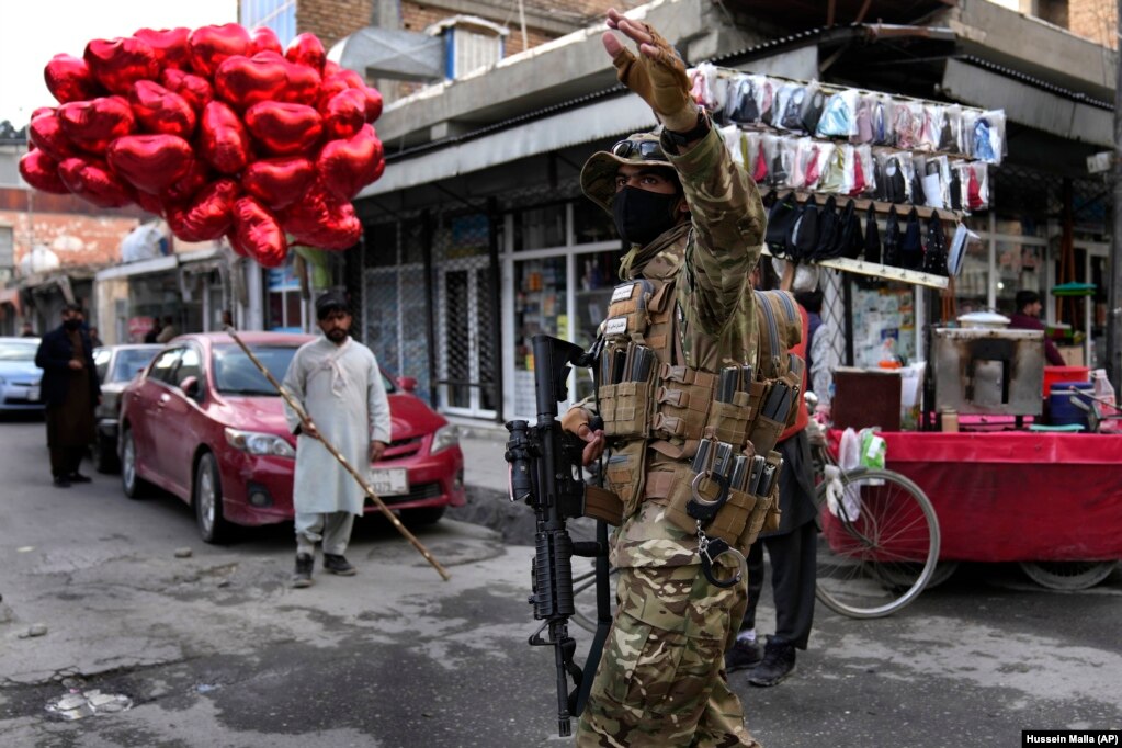 Një luftëtar taliban duke drejtuar komunikacionin, teksa një shitës ambulant priste blerës të balonave në formën e zemrës, për Ditën e Shën Valentinit, në Kabul, Afganistan, më 14 shkurt.