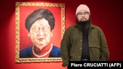 Badiucao poses next to his artwork Carrie Lam 2018, which merges the likeness of Chinese President Xi Jinping with that of Hong Kong leader, at his show in Brescia, Italy. “I wear these attempts at censorship as a badge of honor,” he says.