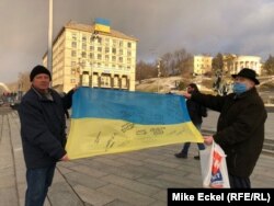 Oleksandr Antonovets, and another man who gave only his first name, Oleksandr, stand on Kyiv’s Independence Square holding a Ukrainian flag with signatures from people who fought in the Donbas against Russia-backed separatists.