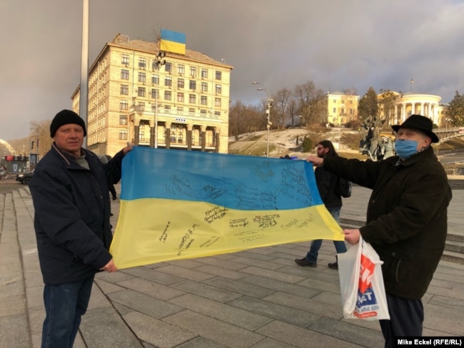 Oleksandr Antonovets, and another man who gave only his first name, Oleksandr, stand on Kyiv’s Independence Square holding a Ukrainian flag with signatures from people who fought in the Donbas against Russia-backed separatists.