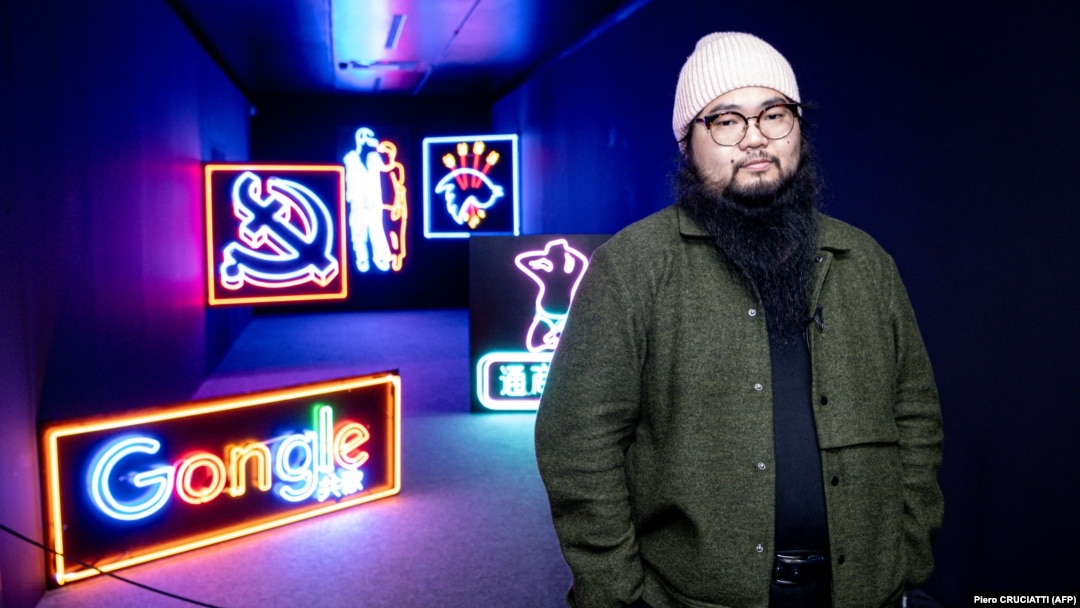 Chinese dissident artist Badiucao poses next to his neon lights artworks series on Hong Kong, in November 2021 at his exhibition in Brescia, Italy.