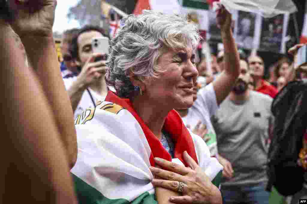 Женщина плачет, стоя вместе с другими членами иранской общины, которые держат плакаты, размахивают флагами и скандируют лозунги во время митинга в Сиднее 1 марта 2026 года. Дэвид Грей / AFP