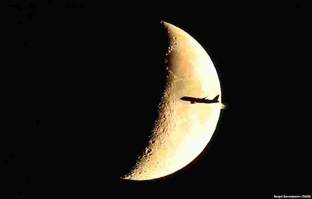 A plane flies past a crescent moon in Moscow, Russia, on June 17.&nbsp;