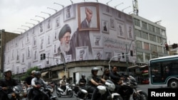 People ride motorcycles near a Tehran billboard with an image of Iran's late supreme leader, Ayatollah Ali Khamenei. 