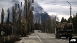 O mașină militară pe fundalul centralei de la Luhansk arzând. 22 februarie 2022, după ce Rusia a recunoscut republicile separatiste