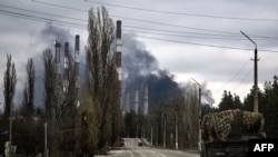 Ukraine - A military vehicle drives on a road as smoke rises from a power plant after shelling outside the town of Schastia, near the city of Lugansk, February 22, 2022.