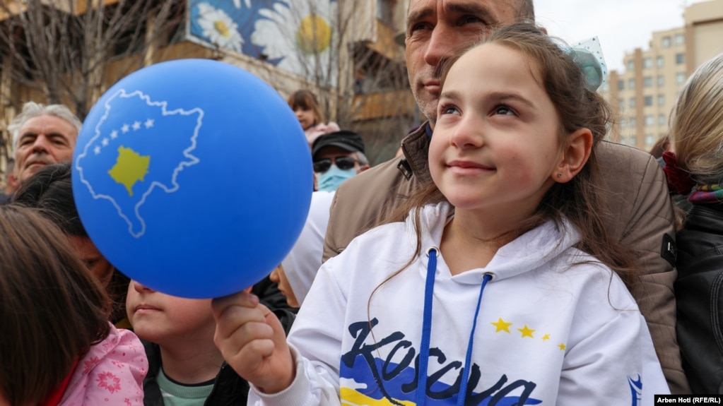 Një vajzë e veshur me një bluzë ku shkruan Kosova, buzëqesh derisa mban një balon me hartën e Kosovës.
