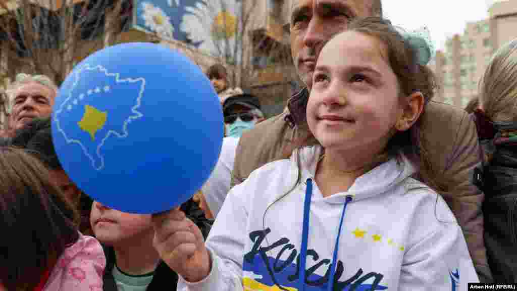 Devojčica u majici na kojoj piše Kosovo i sa balonom u ruci posmatra svečani defile u centru Prištine
