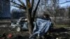 Чалавек накрывае дыванком цела чалавека пасьля бамбаваньня Ўсходняй Украіны каля горда Чугуеў, 22 лютага