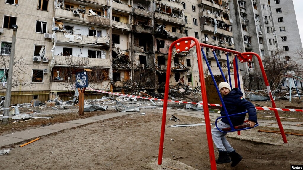 A child sits on a swing in front of a damaged residential building in Kyiv.