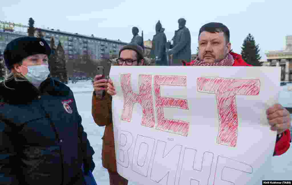 Men hold a sign saying &quot;No to war&quot; in Novosibirsk as a policewoman watches on.&nbsp;