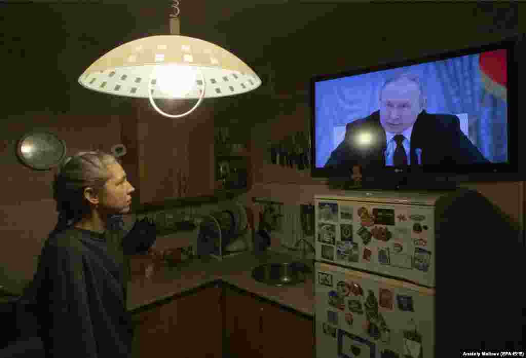 Egy nő nézi a tévében, ahogy Putyin orosz elnök a nemzetbiztonsági tanács ülése után bejelenti, hogy Oroszország elismeri a szakadár régiók függetlenségét