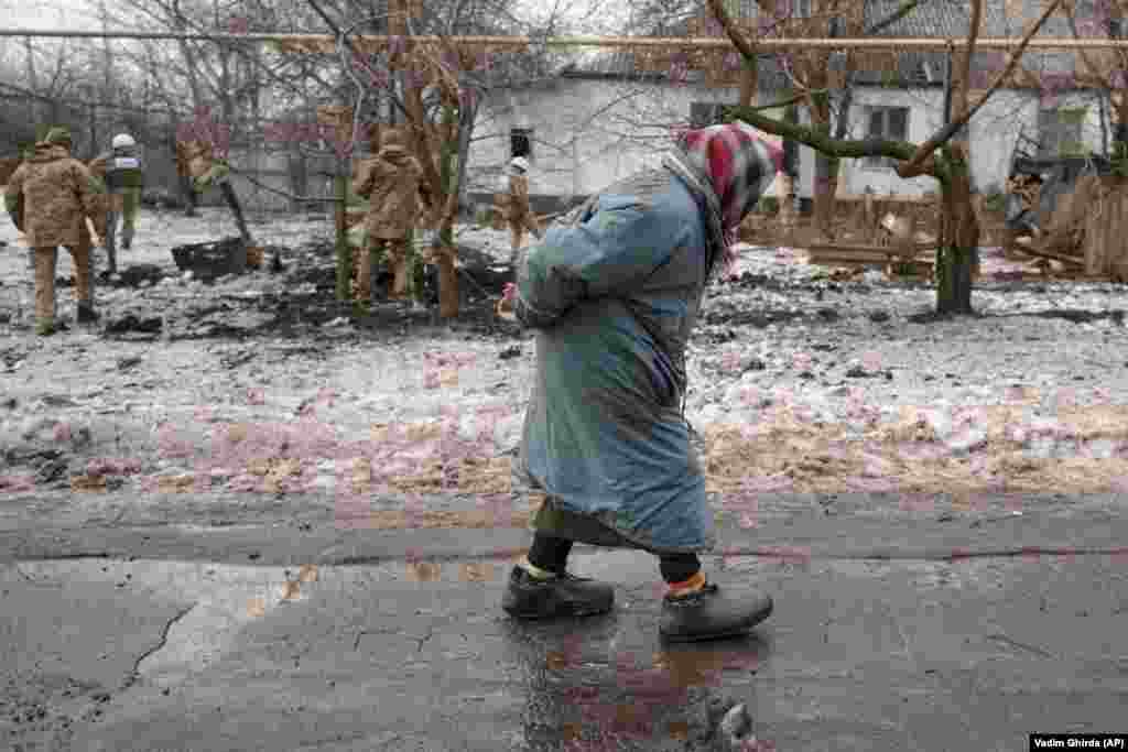 A woman walks by as observers survey a crater and damage to a house from an artillery shell that landed in the front-line town of Vrubivka in eastern Ukraine on February 17.&nbsp;