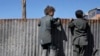 Afghan boys look over a metal barrier at people receiving food supplies during a distribution of humanitarian aid for families in need in Kabul on February 16.