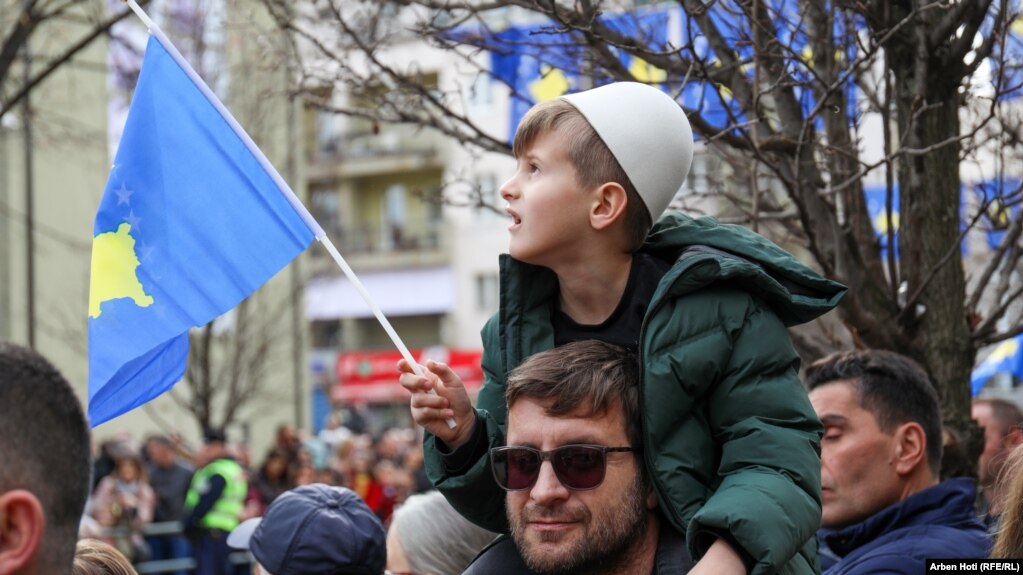 Një fëmijë me plis në kokë mban në dorë flamurin e Kosovës.