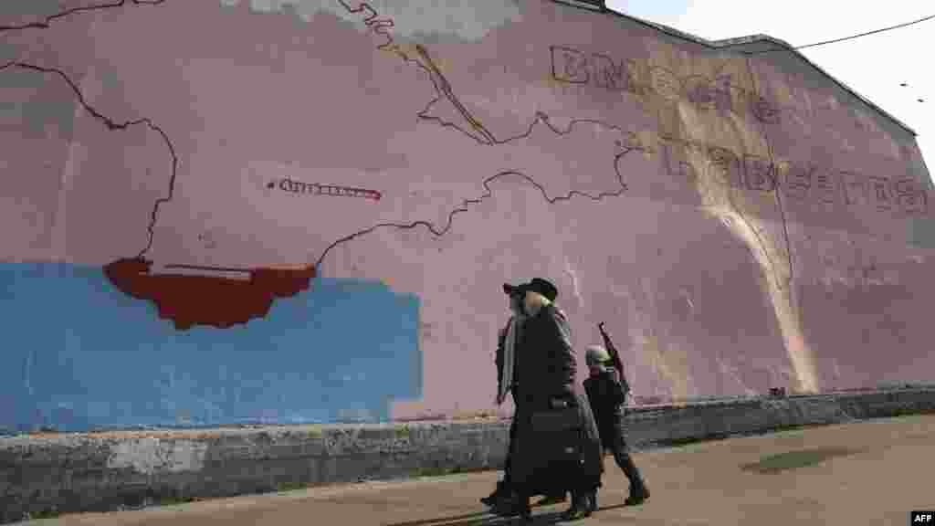 Women and a boy with a toy assault rifle walk past an unfinished wall painting in Moscow depicting a map of the Crimean peninsula and a slogan reading, &quot;Together Forever.&quot; (AFP/Alexander Nemenov)