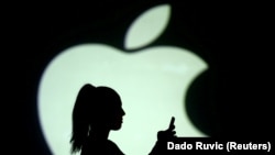 RUSSIA -- Silhouette of a mobile user seen next to a screen projection of the Apple logo - generic