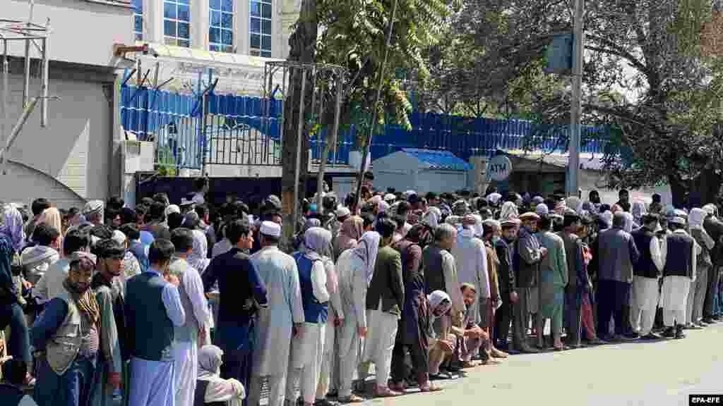 Zeci de oameni stau la coadă în fața unei bănci pentru a retrage bani. După retragerea trupelor americane din Afganistan, băncile s-au deschis sub anumite condiții, oamenii având voie să retragă 200 USD din cont pe săptămână și doar de la sucursalele centrale din Kabul.