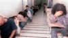 While covering their faces, Iranian youth who had been arrested in student protests, sit in a hallway of the Evin prison, in Tehran, Iran, Sunday, June 15, 2003.