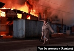 Жінка проходить повз палаючий будинок на місці повітряного удару армії РФ в місті Бровари на Київщині, 14 березня 2026 року